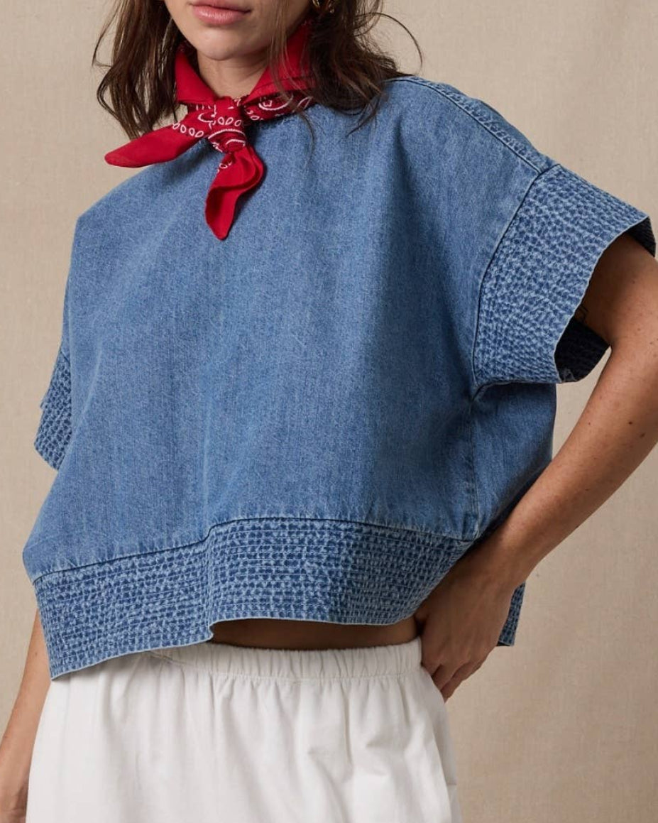 Woman wearing a blue top and white pants with a red scarf around her neck against a beige background