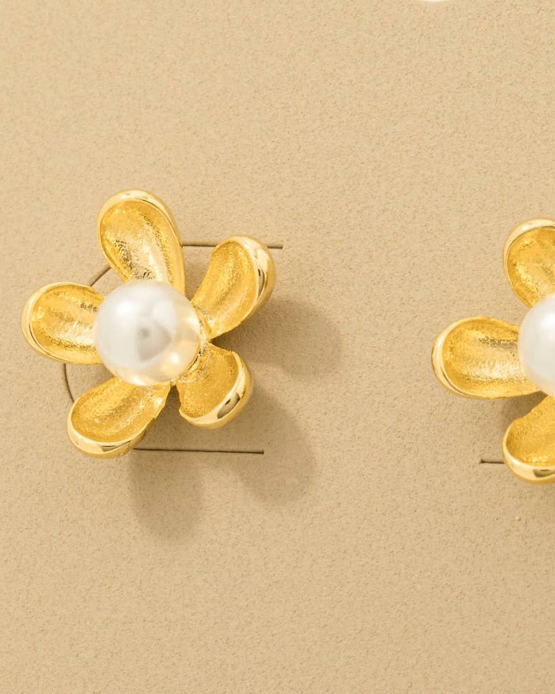 Gold flower-shaped earrings with pearl centers on a beige background