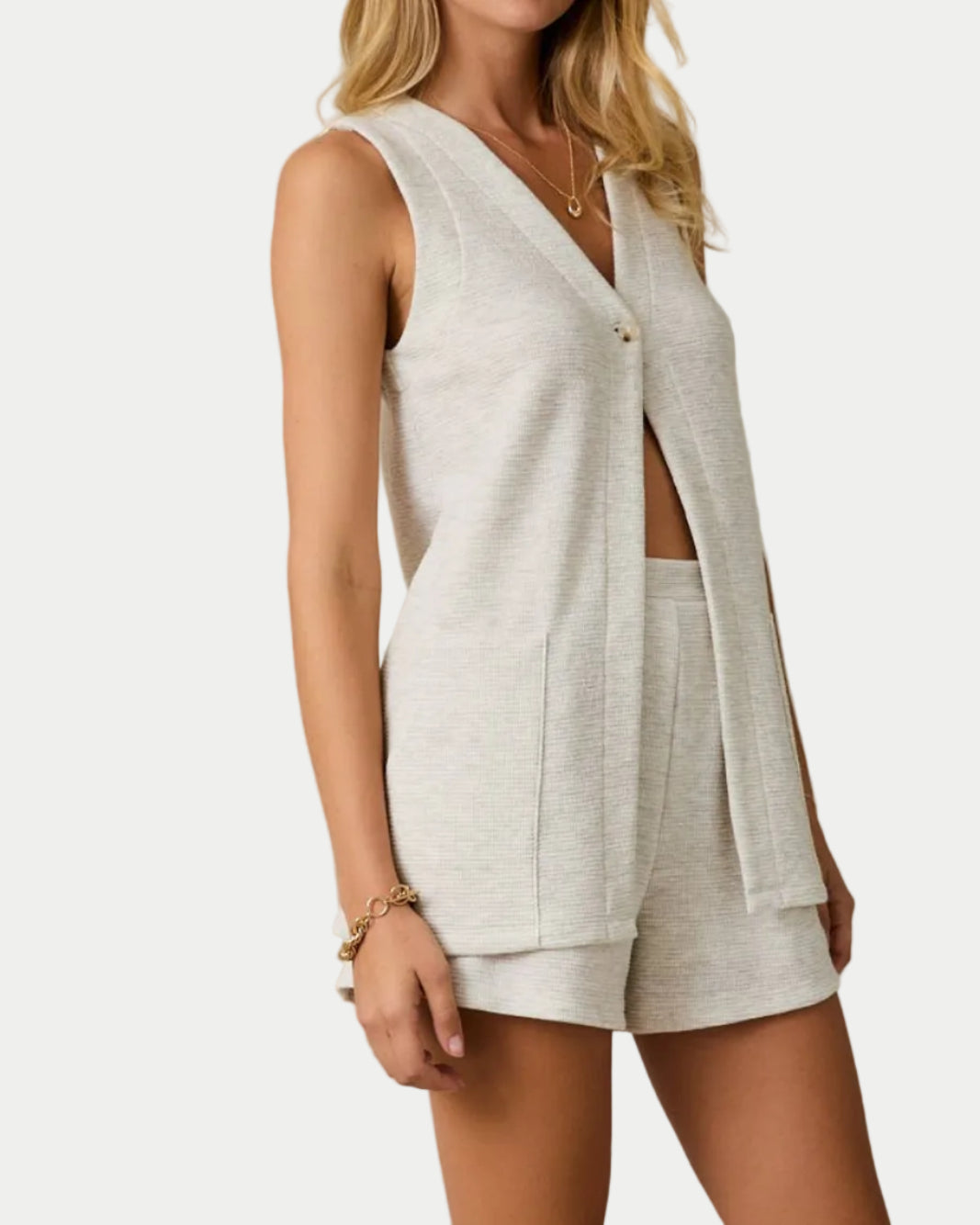 Woman wearing a white sleeveless top and shorts against a plain background