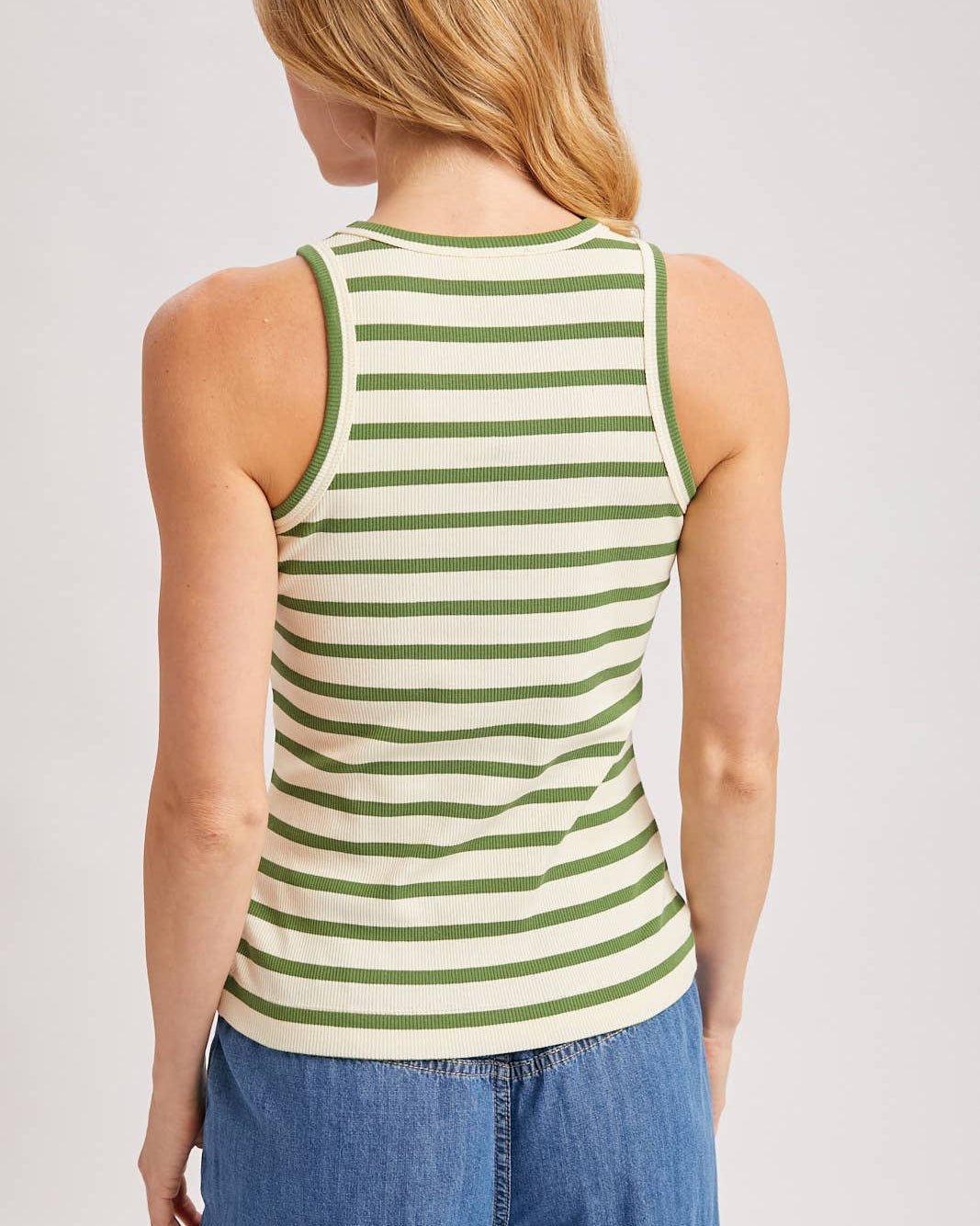 Person wearing a green and white striped tank top with blue jeans on a plain background