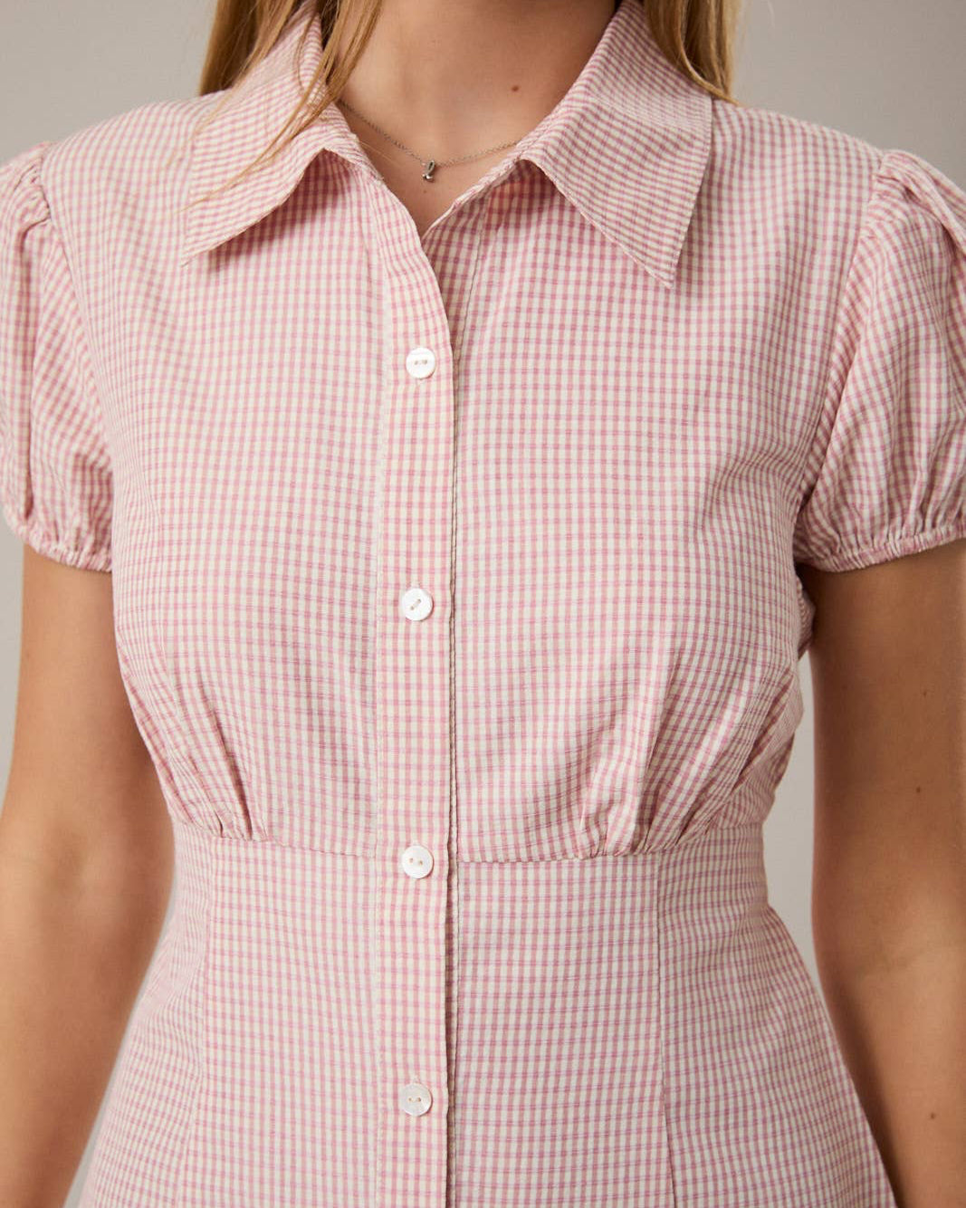 Close-up of a person wearing a pink checkered dress against a neutral background