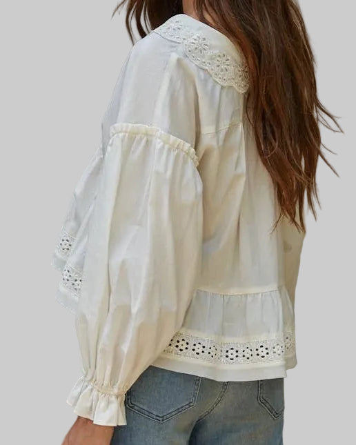 Woman wearing a white blouse with lace details against a neutral background