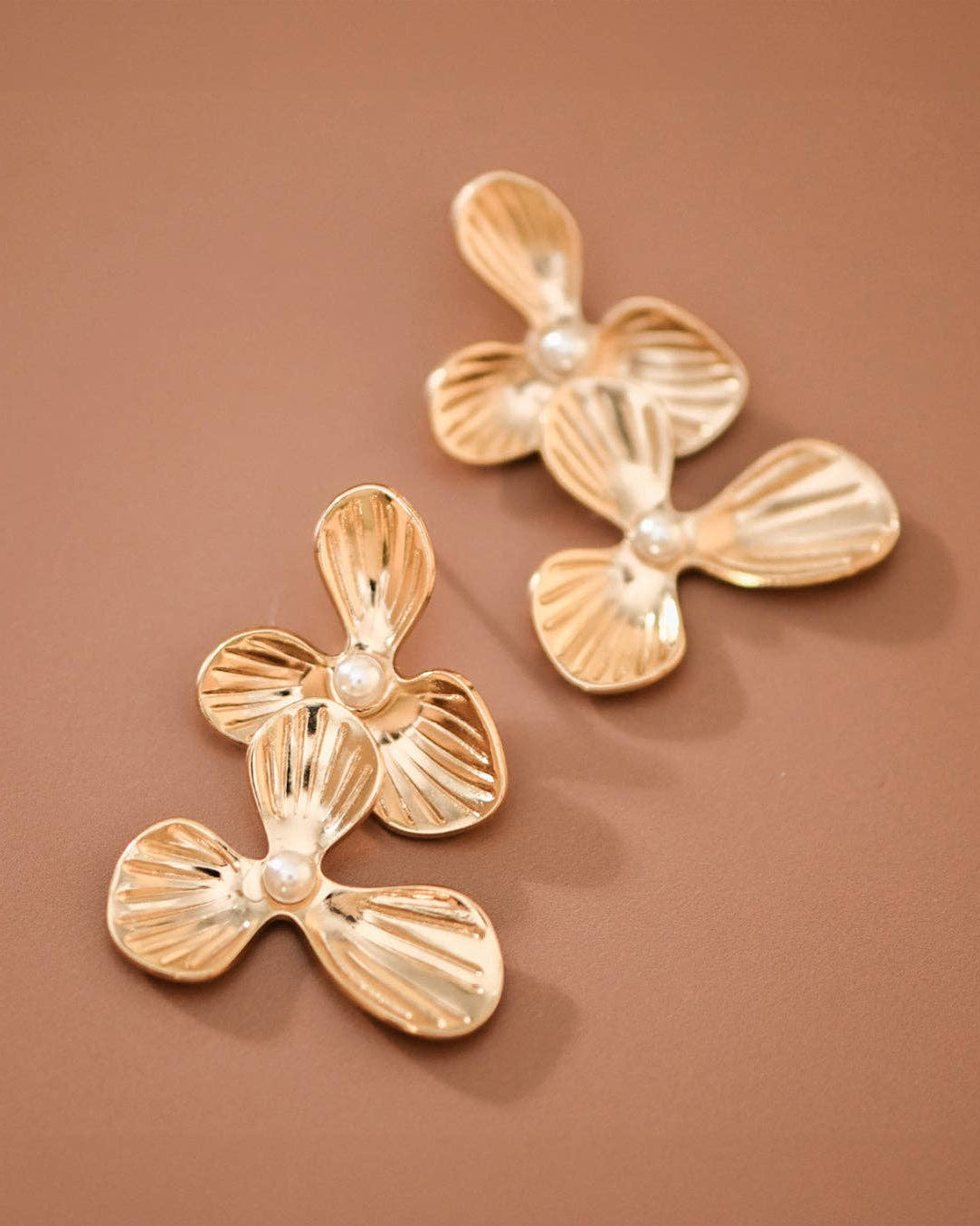 Pair of gold earrings with pearl-like centers on a brown background