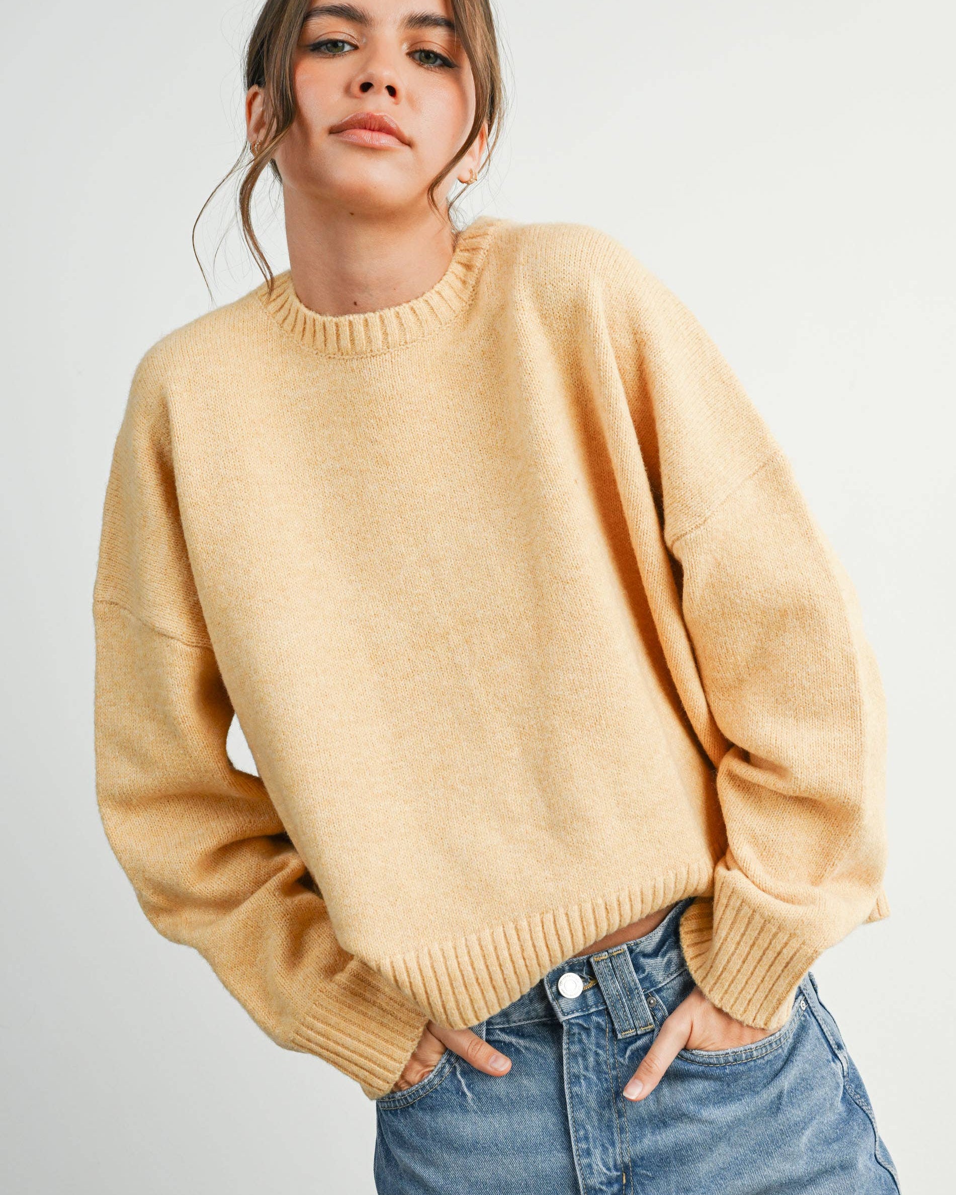 Woman wearing a beige sweater and blue jeans against a white background