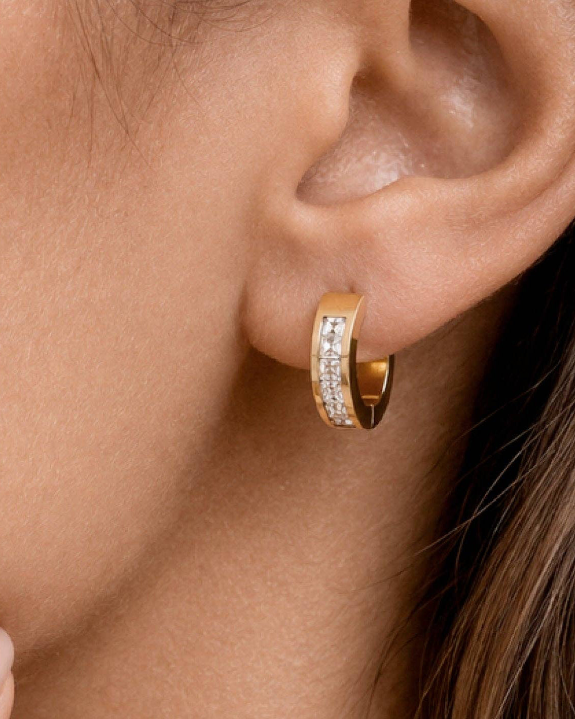 Gold hoop earring with embedded diamonds worn by a person