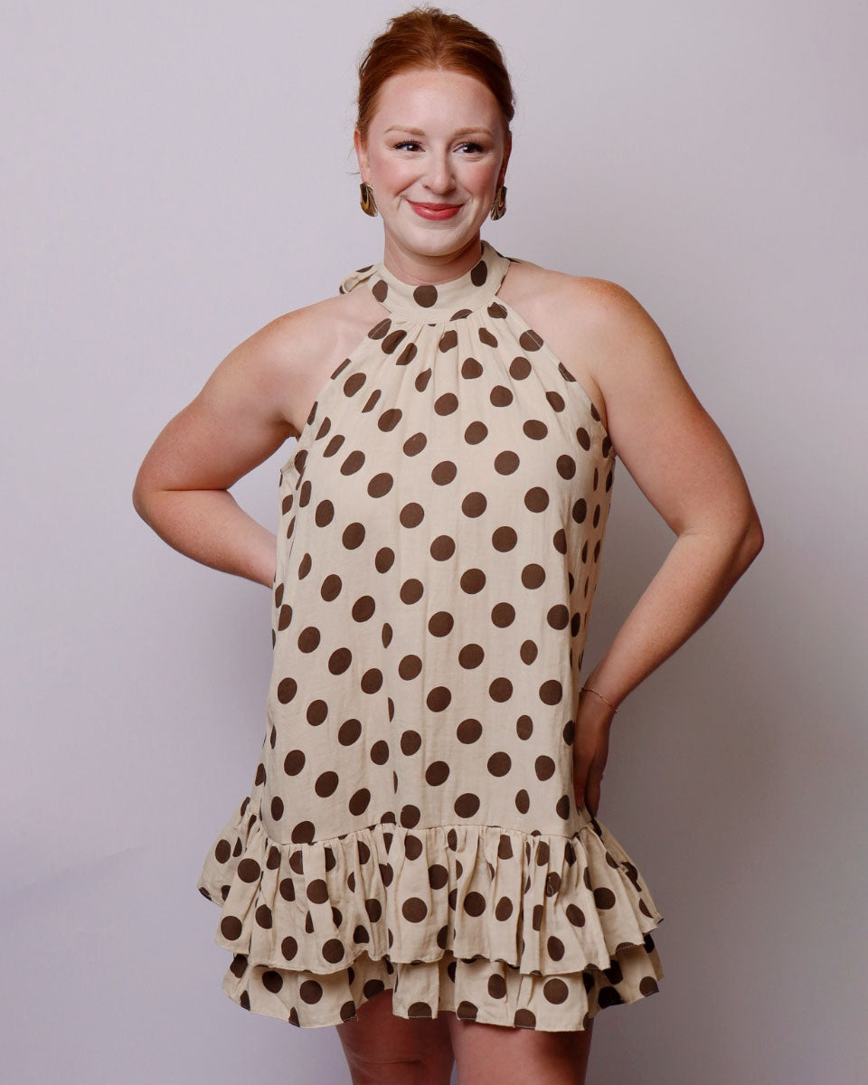 Woman wearing a beige dress with brown polka dots against a plain background