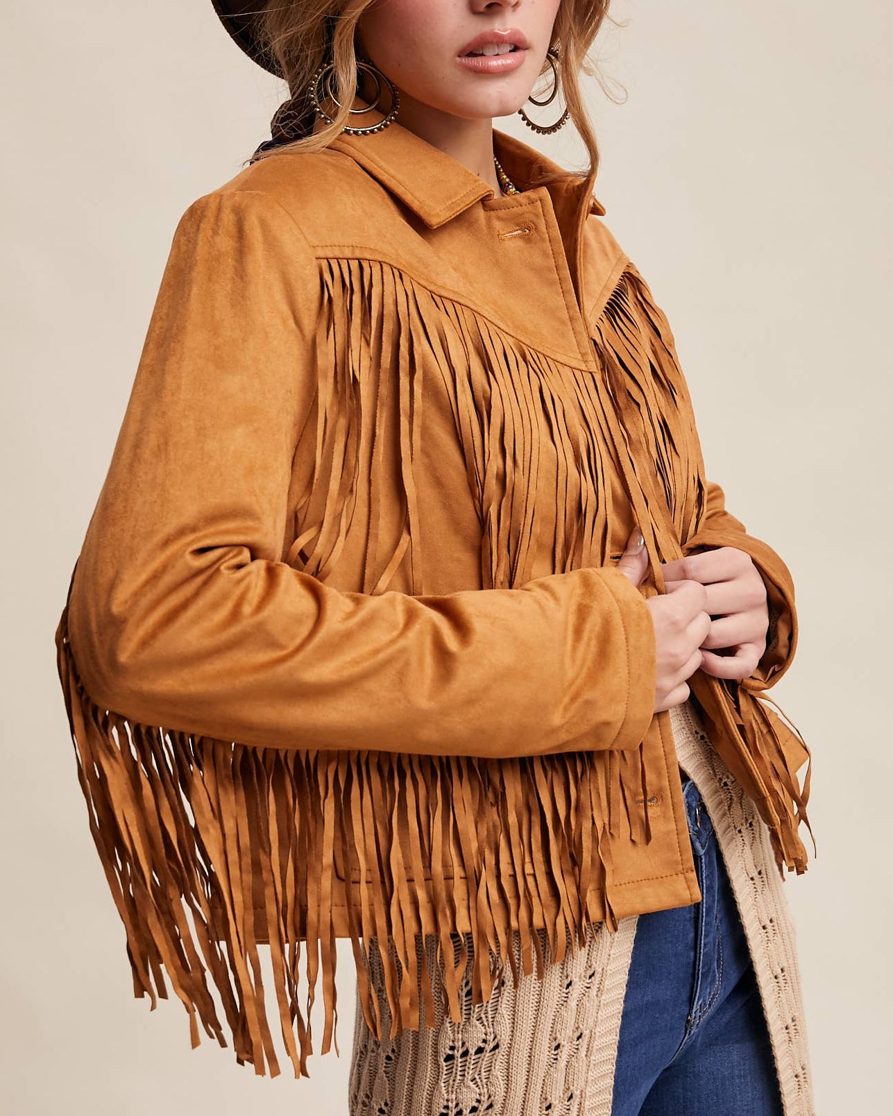 Woman wearing a brown fringed jacket and cowboy hat against a beige background
