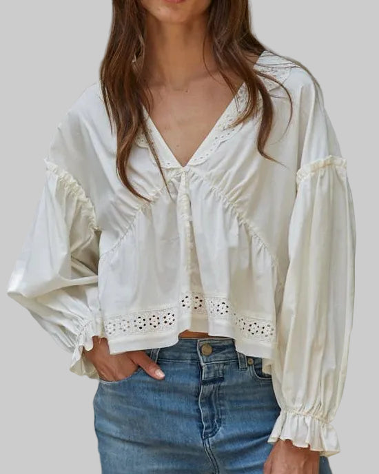 Woman wearing a white blouse with lace details and blue jeans against a plain background