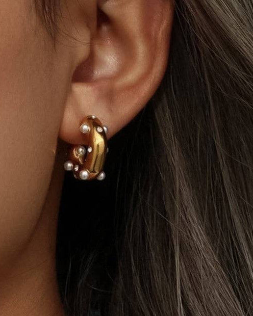 Close-up of an ear wearing a gold earring with pearls.