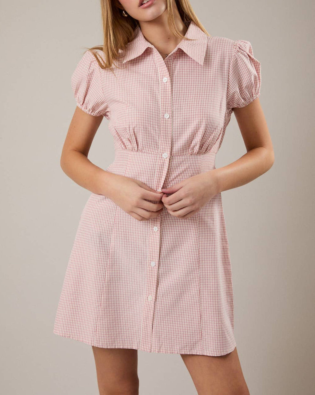 Woman wearing a pink checkered dress against a neutral background