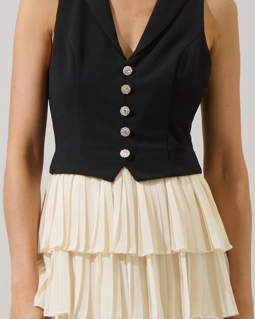 Black sleeveless top with silver buttons and a cream ruffled skirt on a neutral background