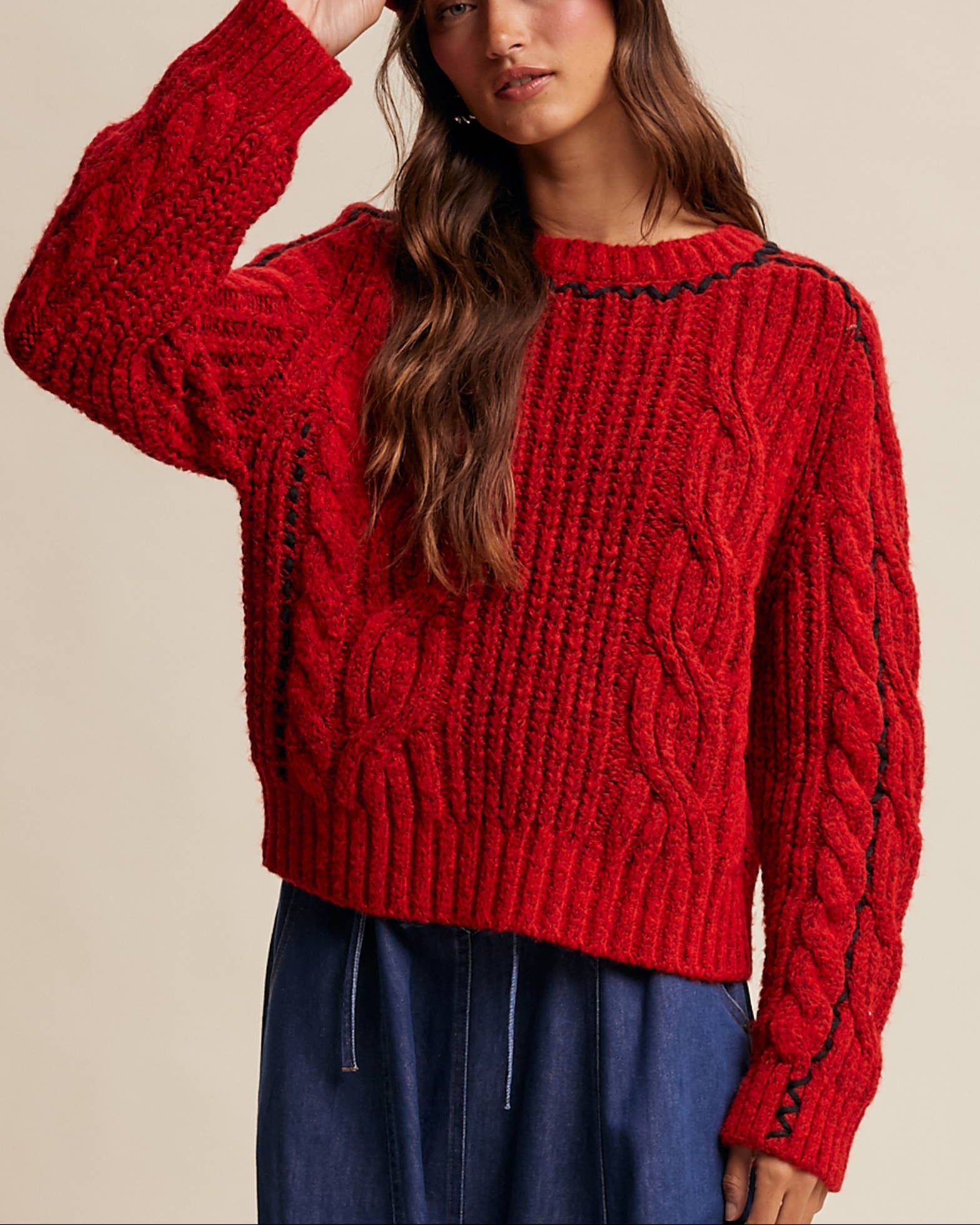 Woman wearing a red knitted sweater and matching red cap against a beige background