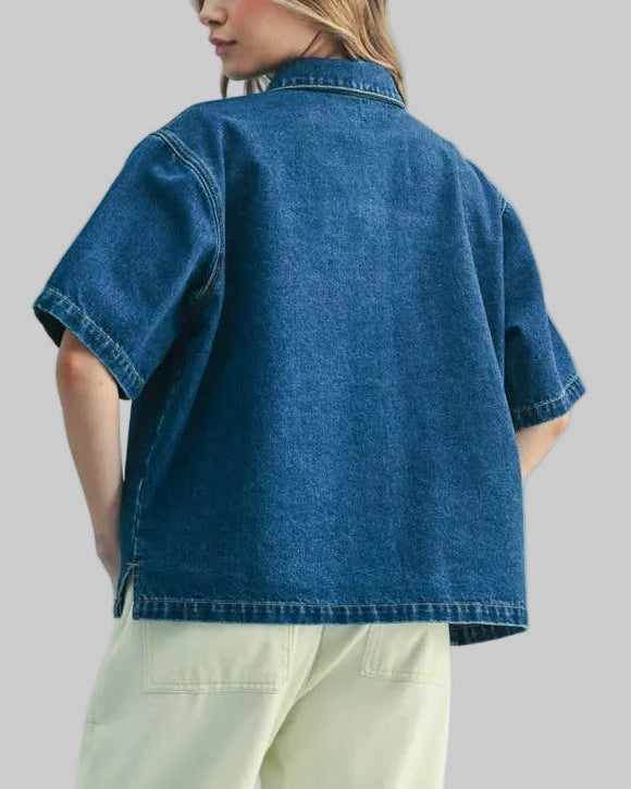 Person wearing a denim shirt and light-colored pants on a plain background