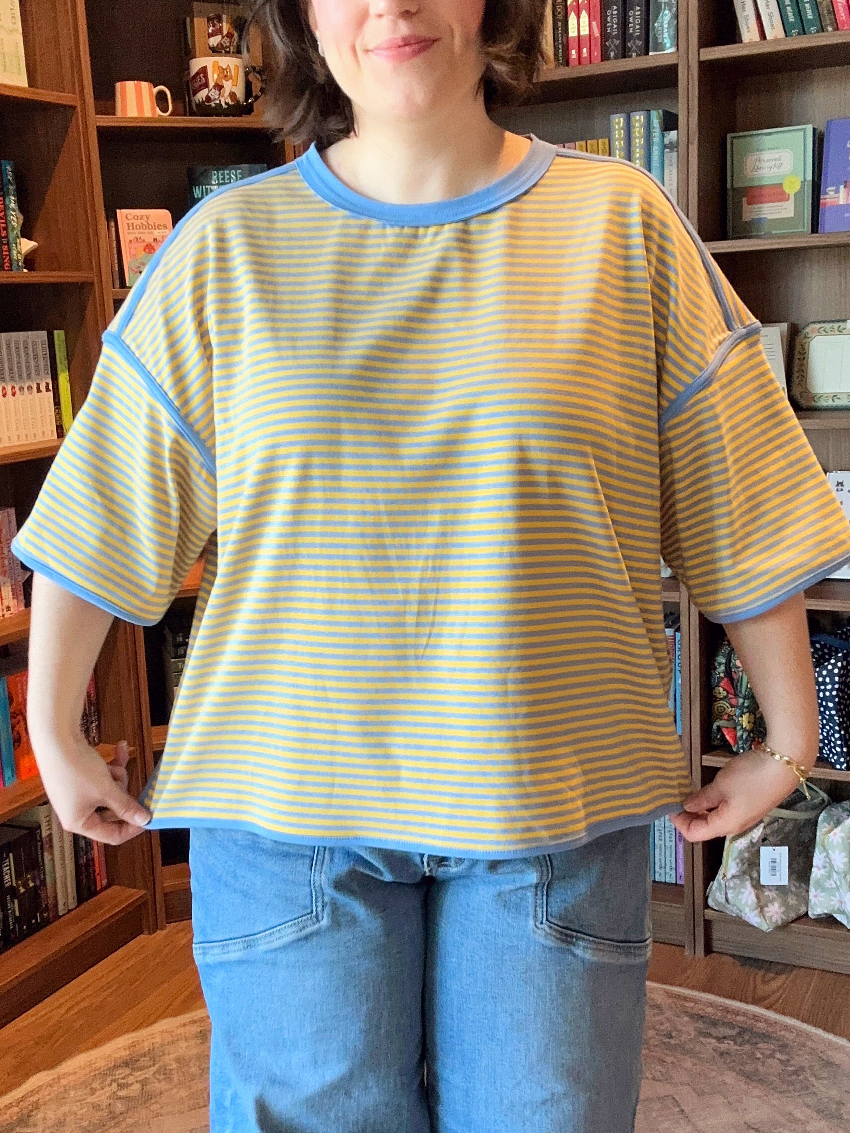 Person wearing a yellow and blue striped shirt in front of a bookshelf