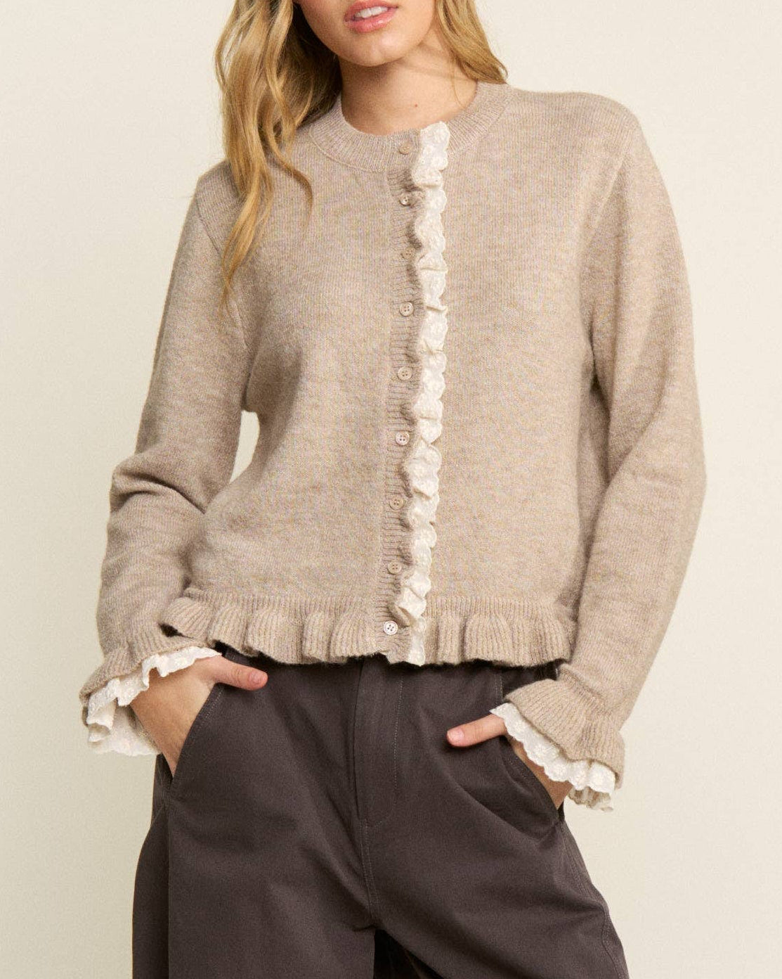 Woman wearing a beige cardigan with lace trim and brown wide-leg pants on a white background