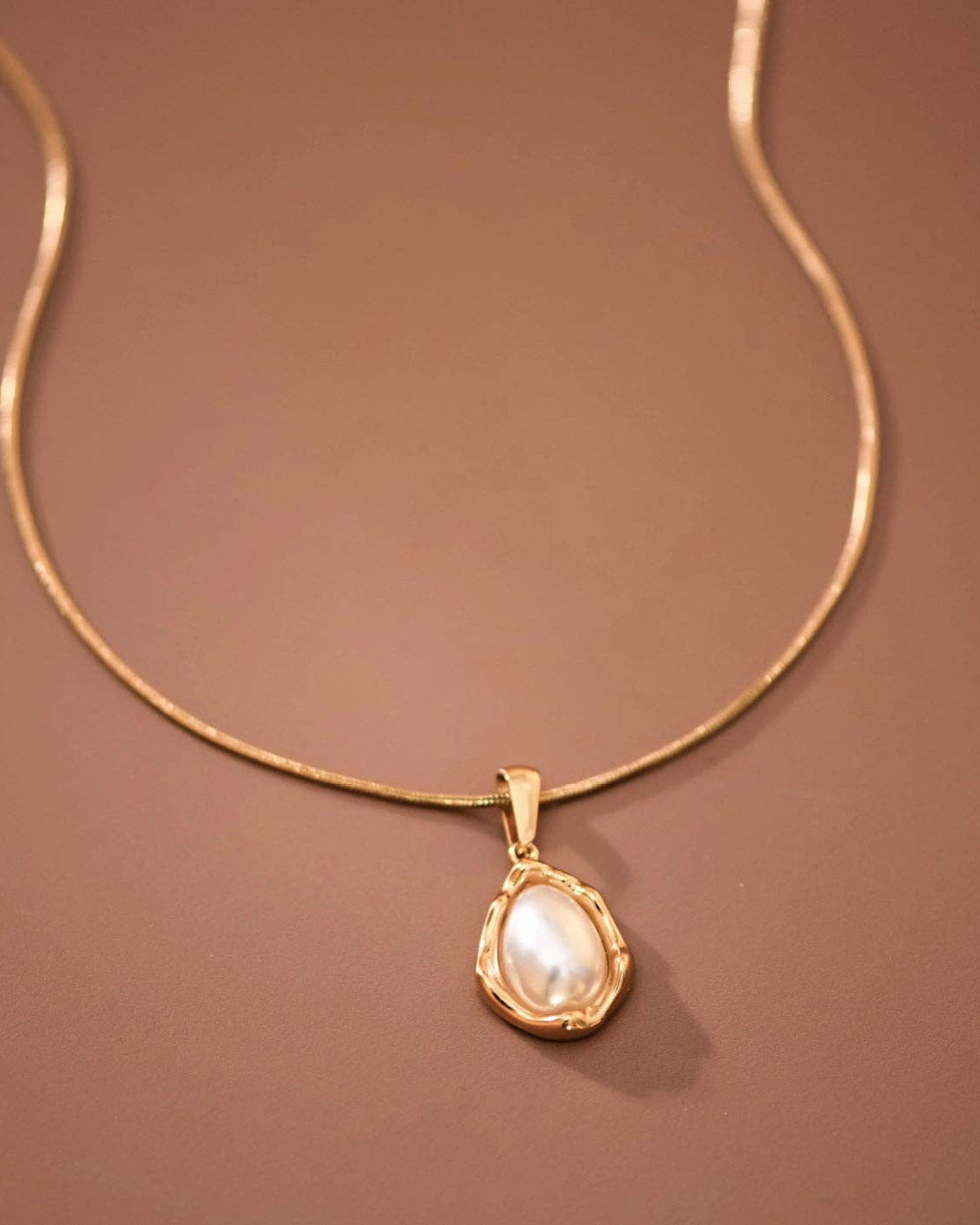 Gold necklace with a teardrop-shaped pearl pendant on a brown background