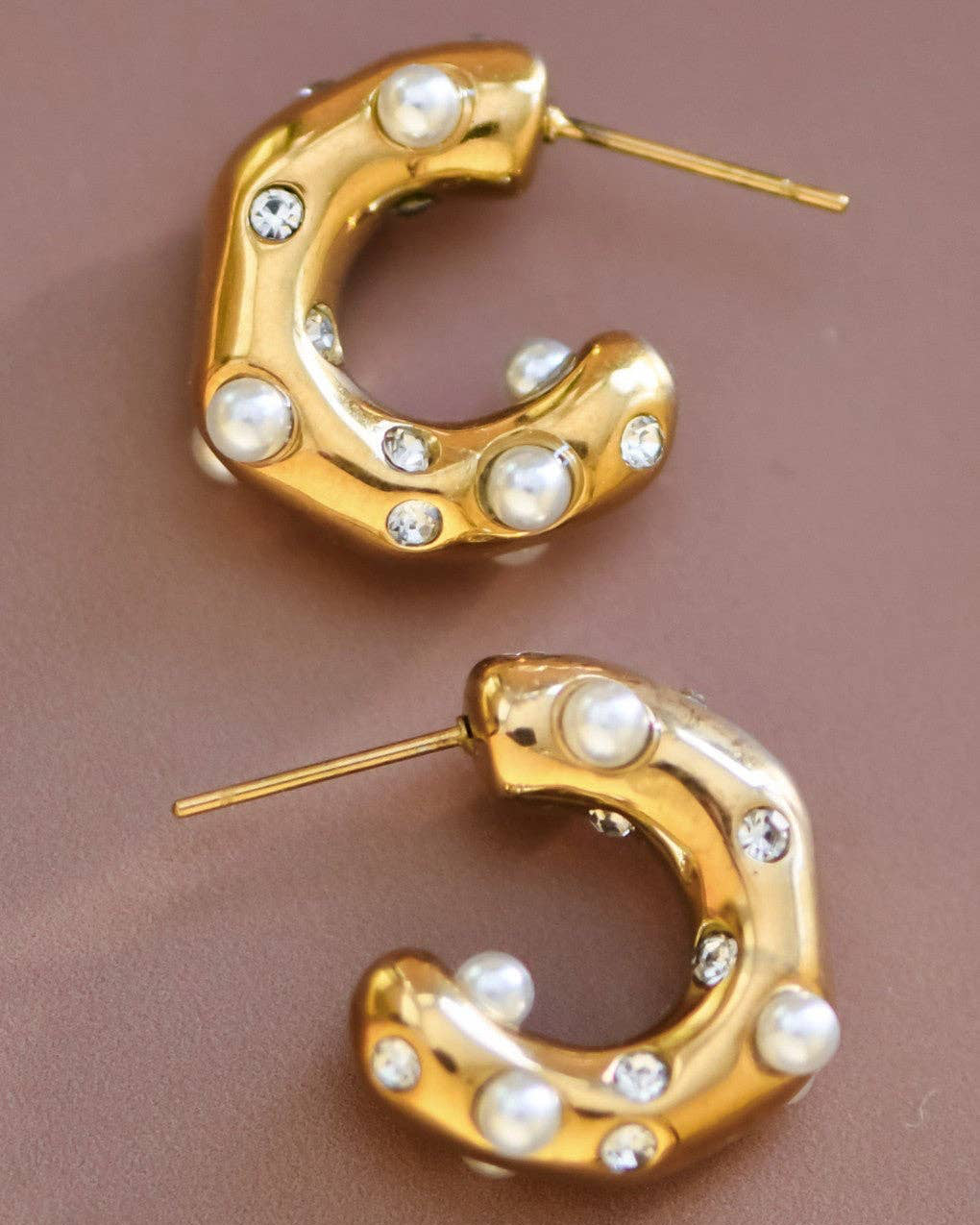 Gold hoop earrings with pearls and crystals on a brown background