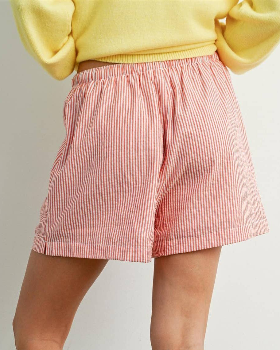 Person wearing red striped shorts and black rain boots on a plain background