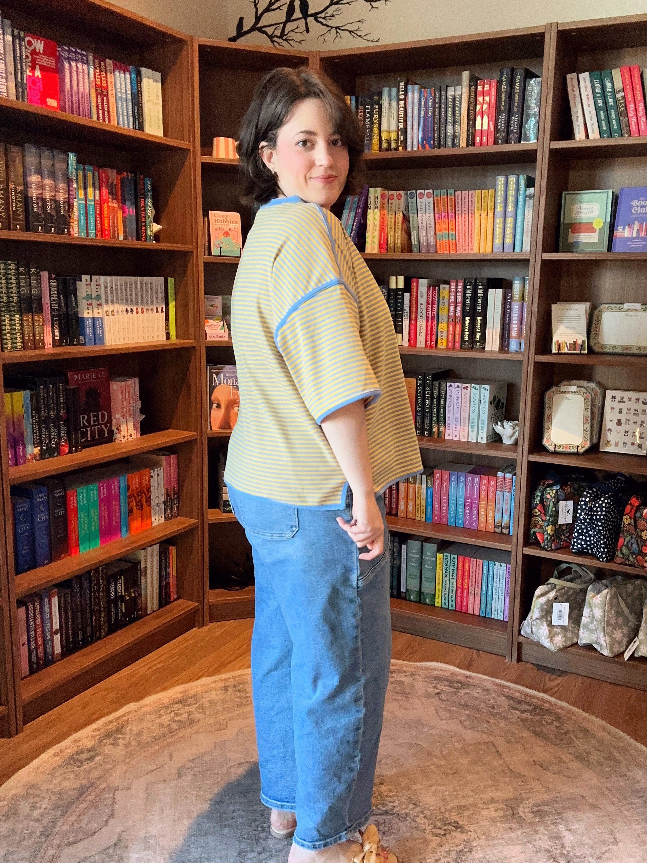 Person standing in a room with bookshelves filled with books and bags.