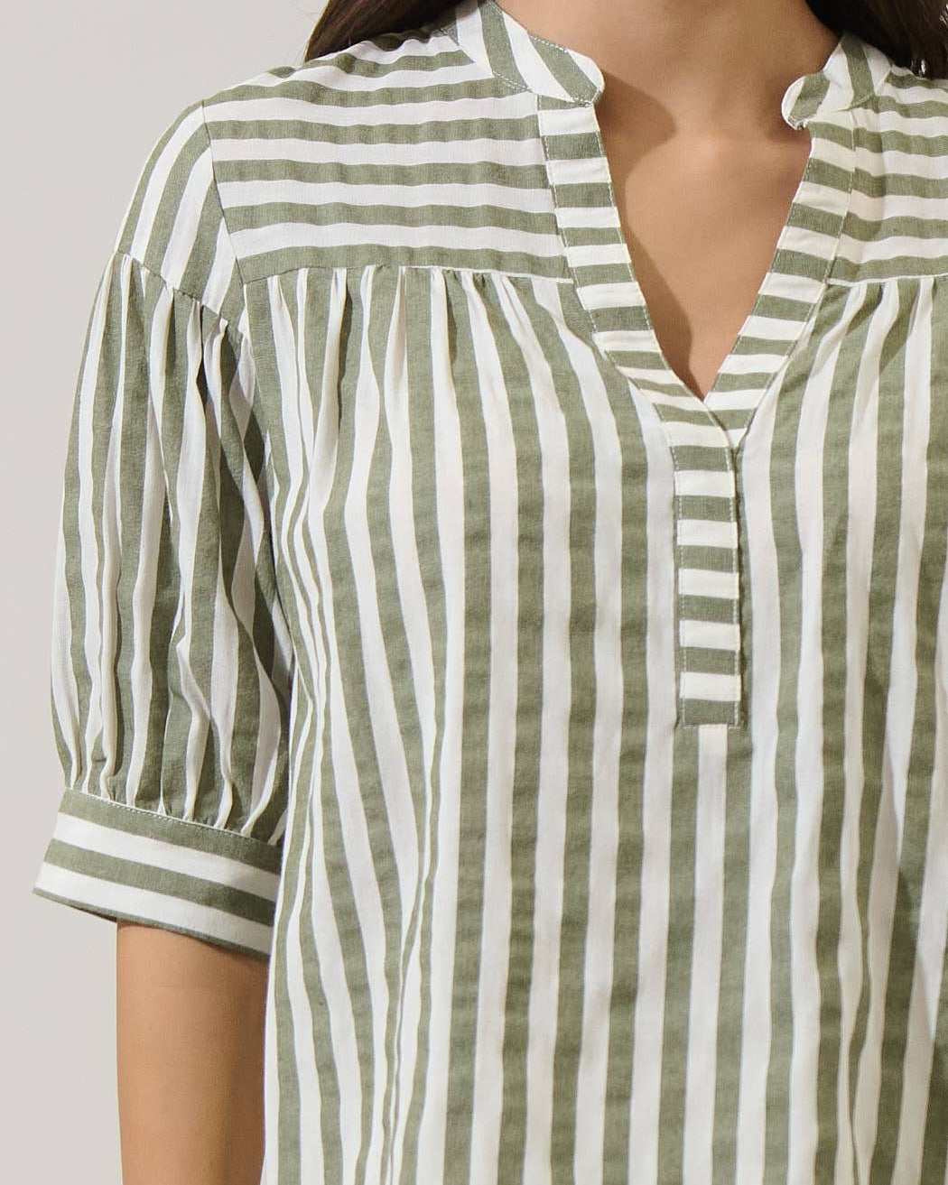 Green and white striped shirt worn by a person on a plain background