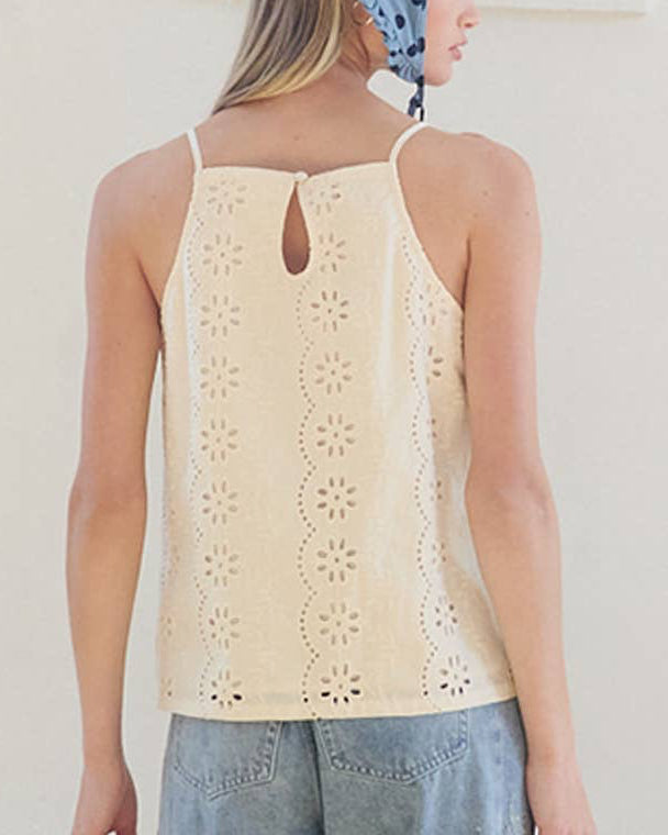 Woman wearing a beige sleeveless top and blue jeans with a blue polka dot headscarf indoors.