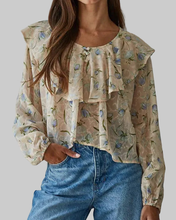 Woman wearing a floral blouse with ruffled sleeves and blue jeans against a gray background