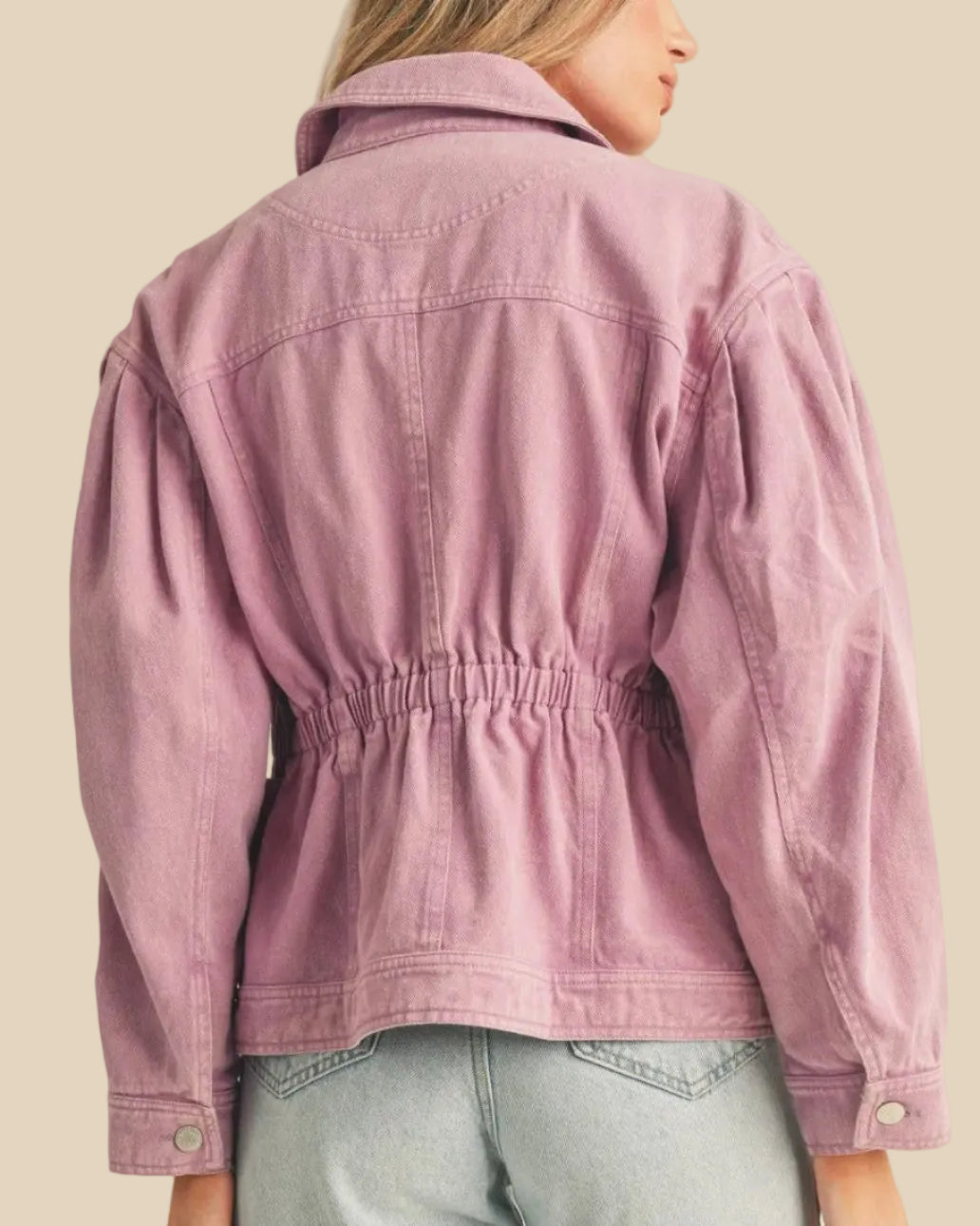 Person wearing a light purple jacket and light blue jeans on a beige background