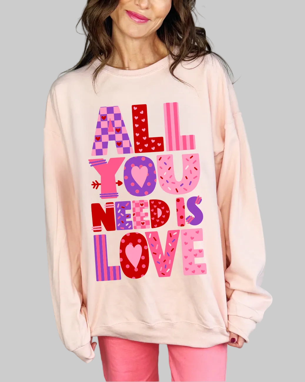 Woman wearing a pink sweatshirt with 'All You Need Is Love' text in various colors.