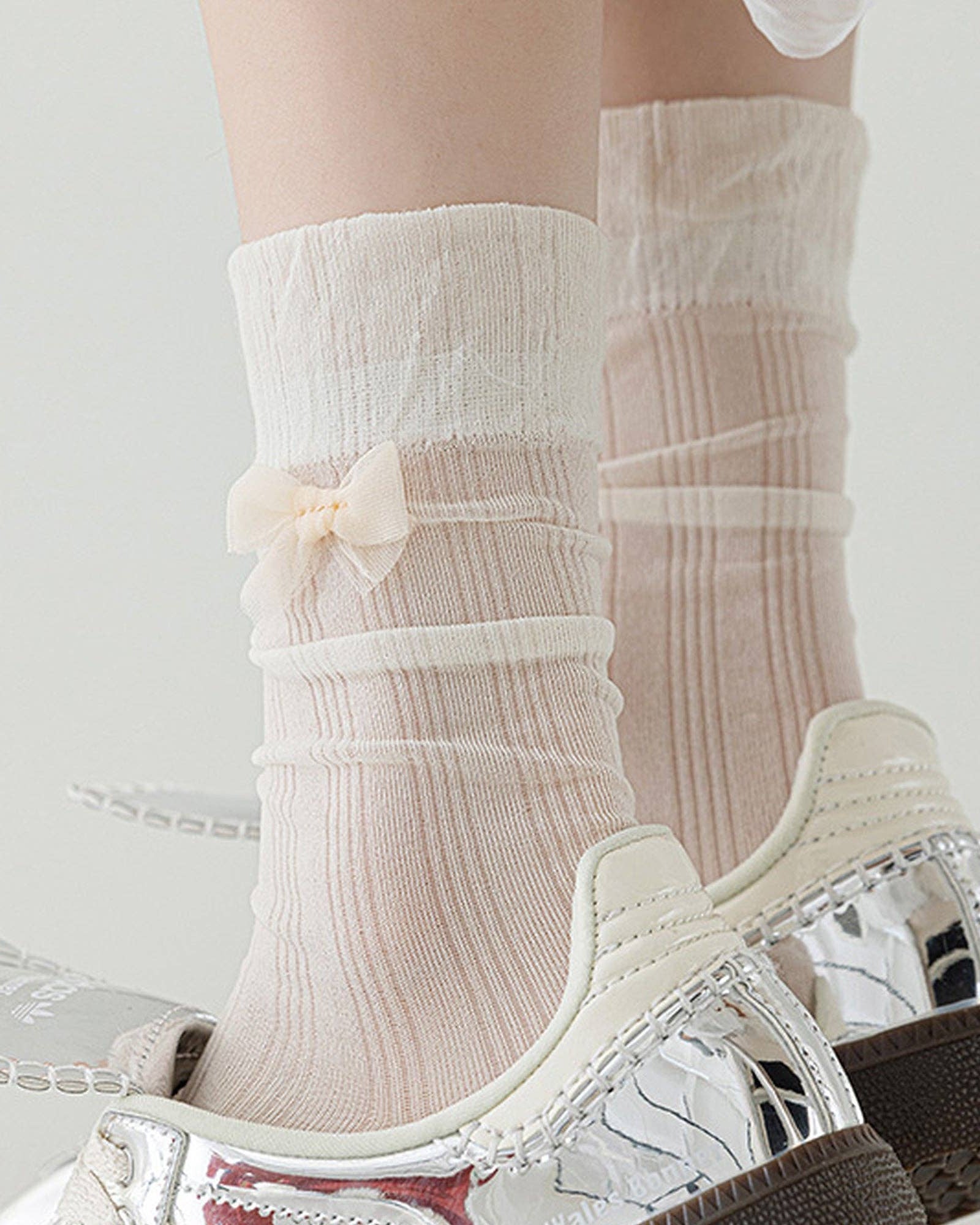 White socks with a bow detail worn with transparent high-heeled shoes on a light background