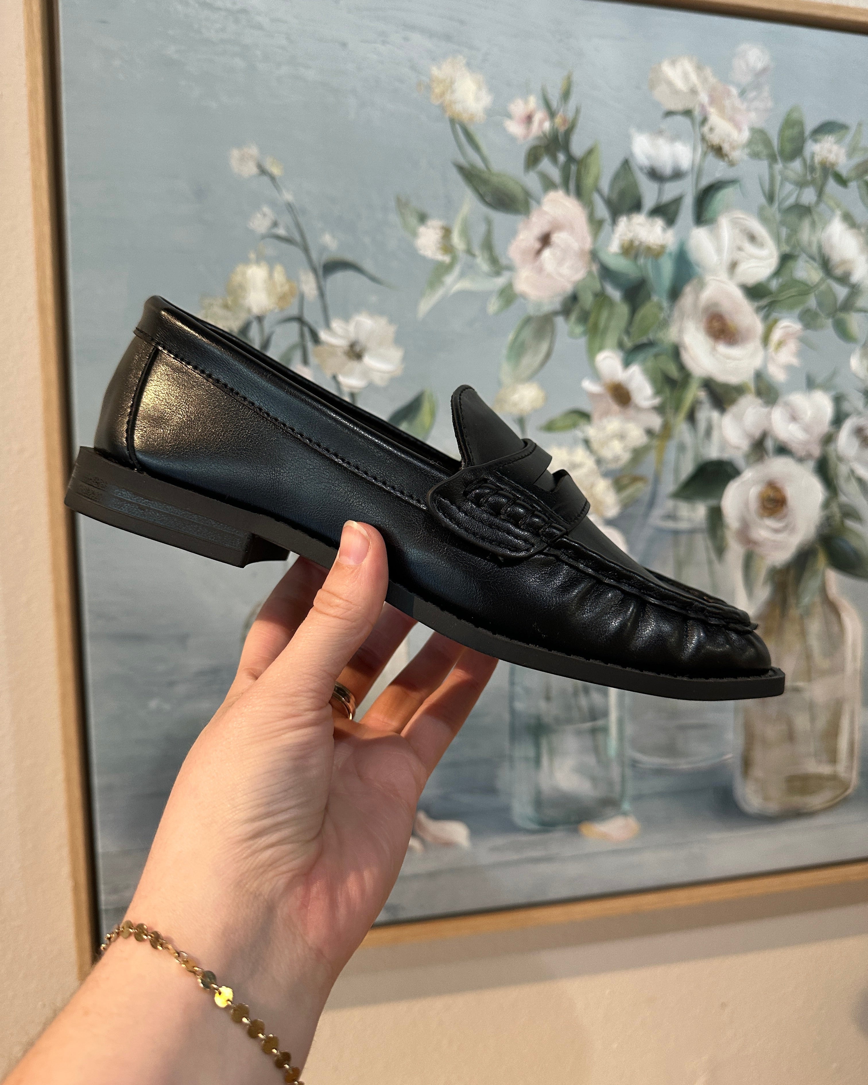 Black shoe held by a hand in front of a floral painting