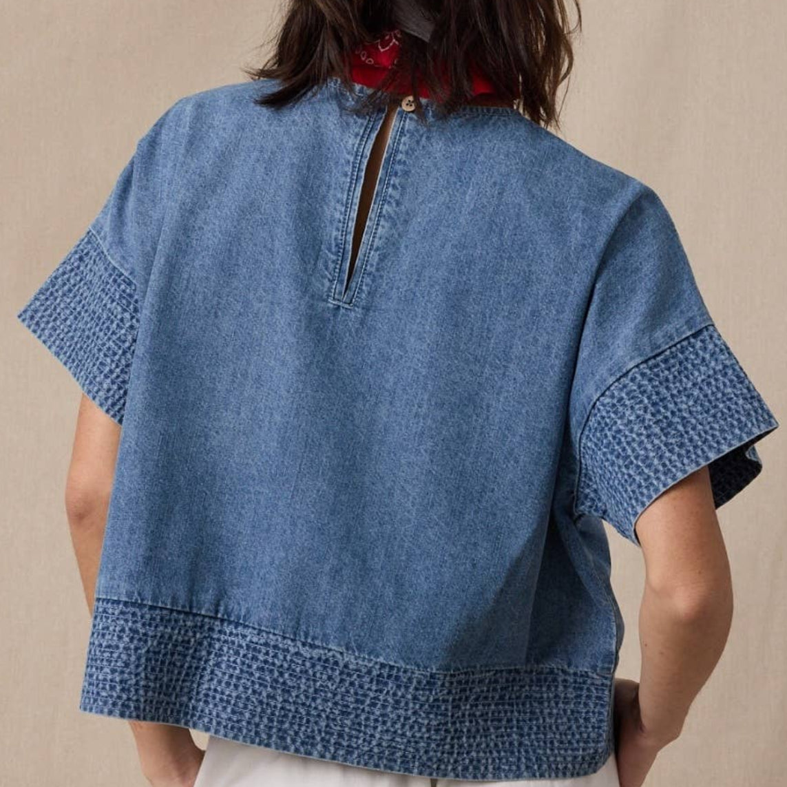 Person wearing a blue denim shirt with white pants against a beige background