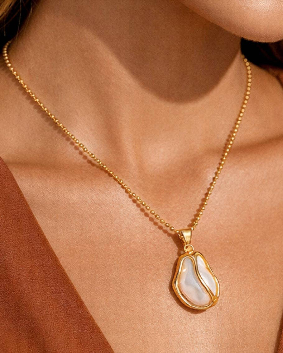 Gold necklace with a pendant on a person wearing a rust-colored garment