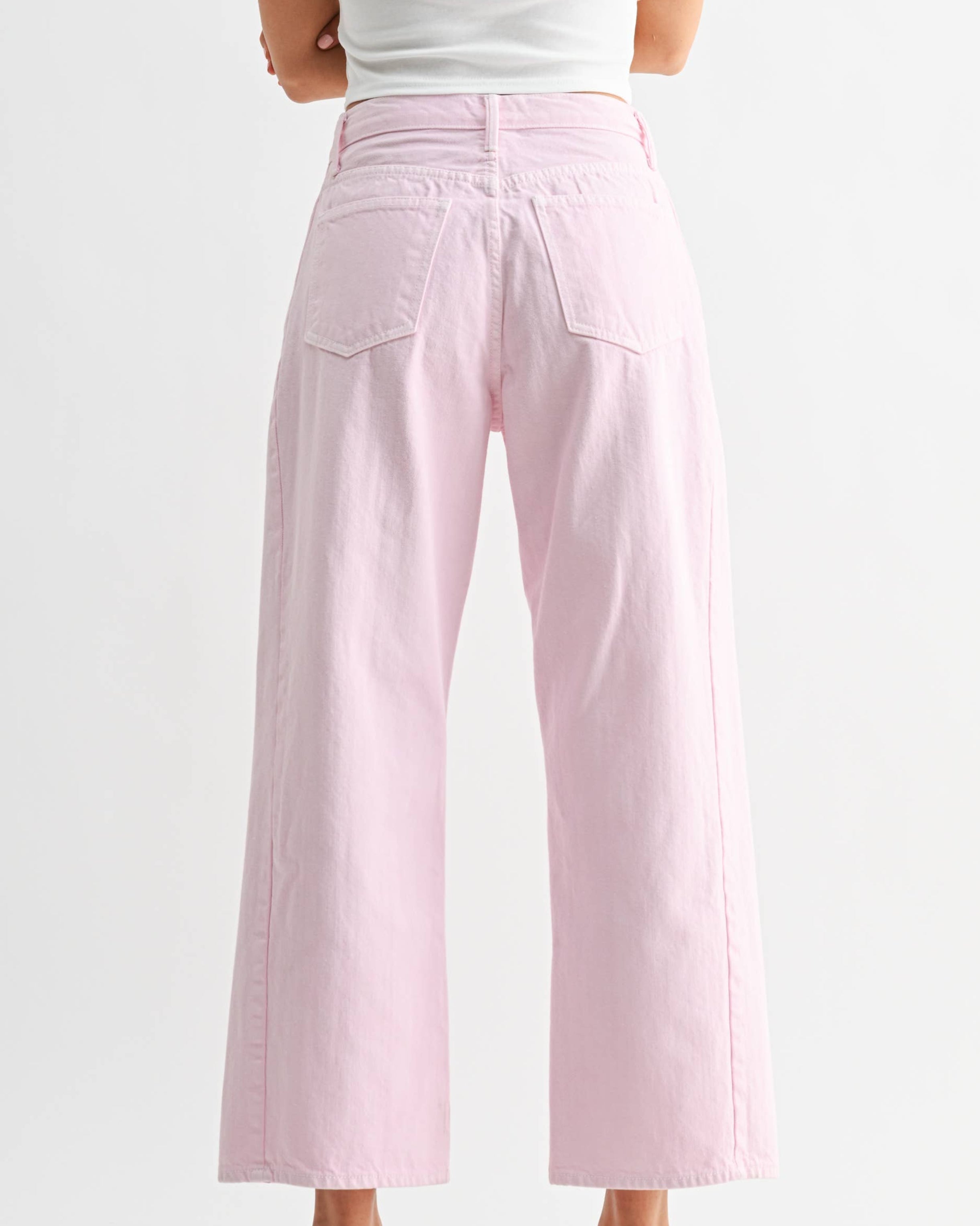 Woman wearing light pink pants and a white top on a plain background