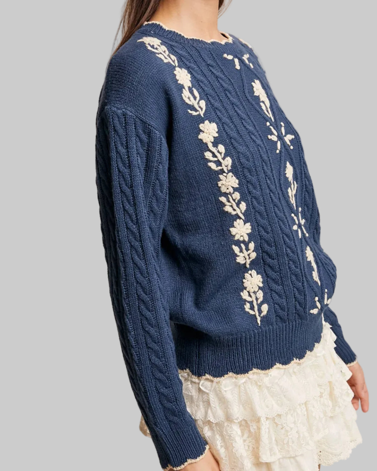 Woman wearing a blue sweater with floral embroidery on a neutral background
