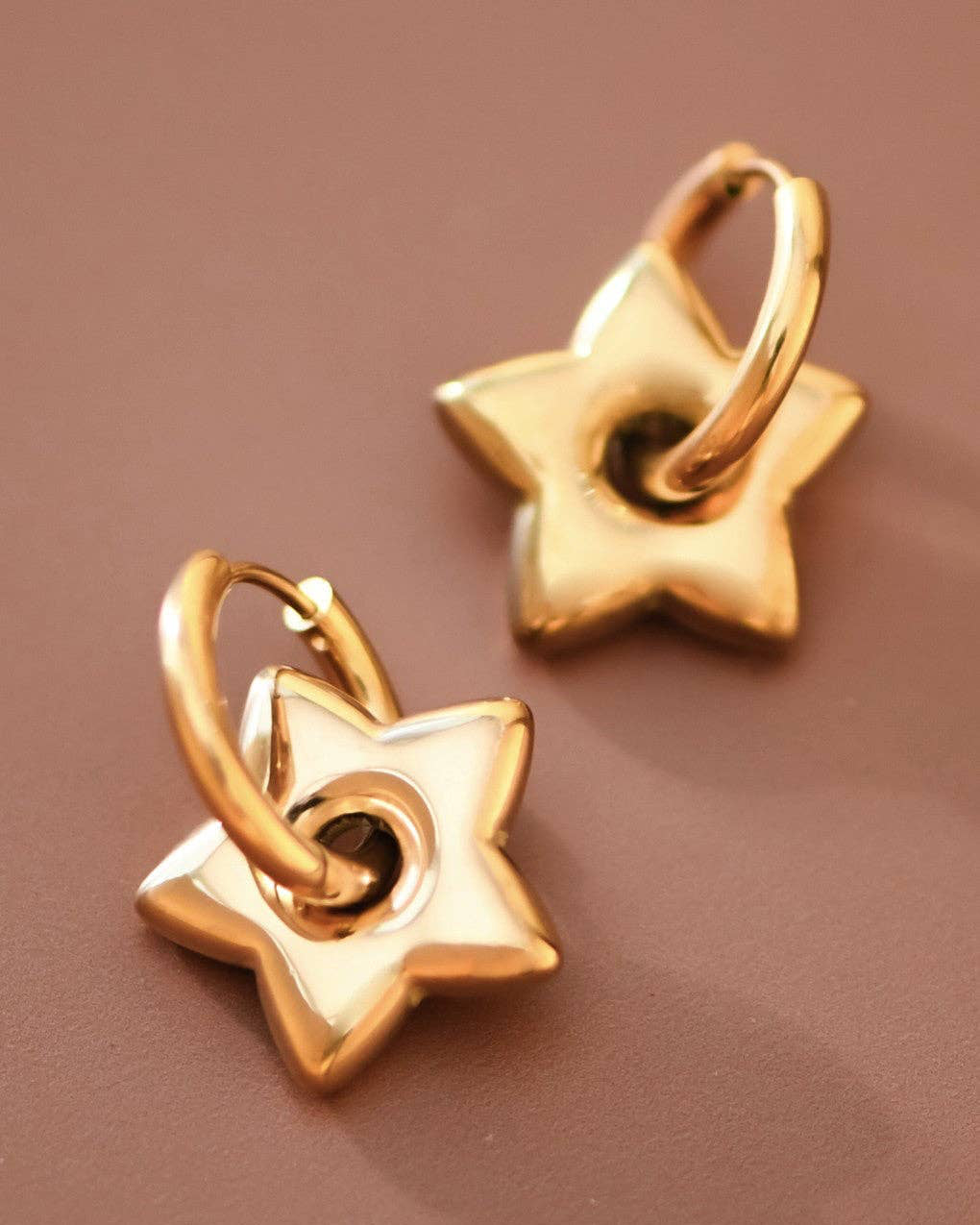 Pair of gold star-shaped earrings on a brown background