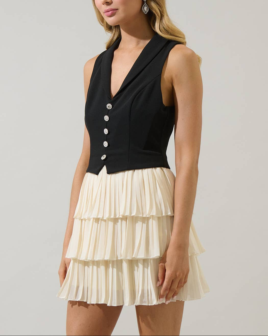 Woman wearing a black sleeveless cardigan over a cream skirt against a plain background