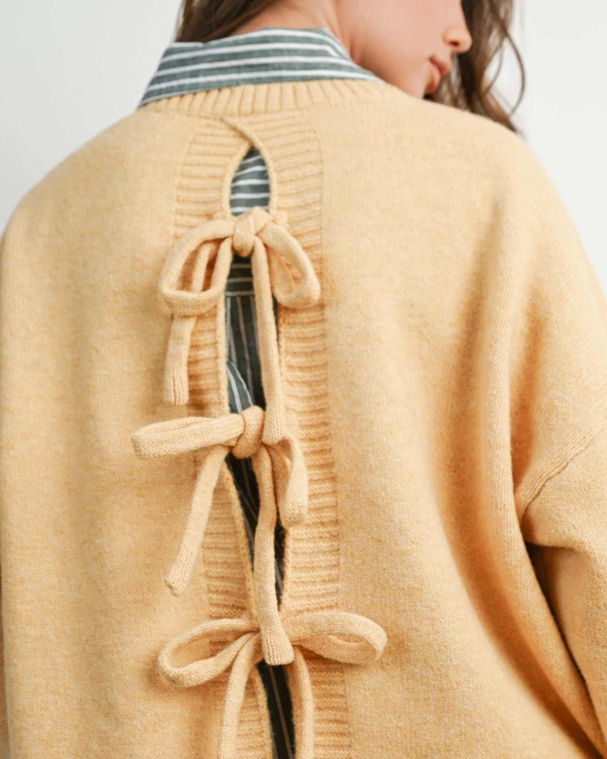 Woman wearing a beige cardigan with bow details on a plain background