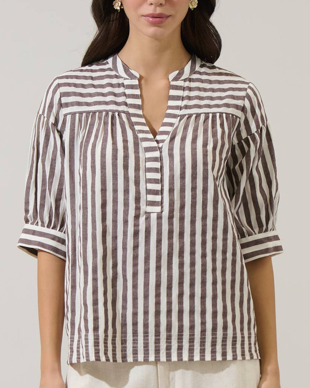 Woman wearing a striped shirt and white pants against a plain background