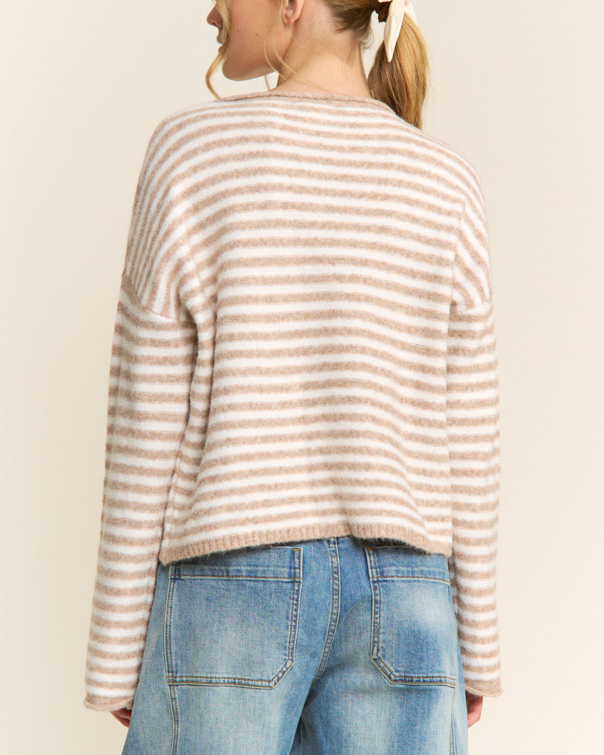 Person wearing a striped sweater and blue jeans against a plain background
