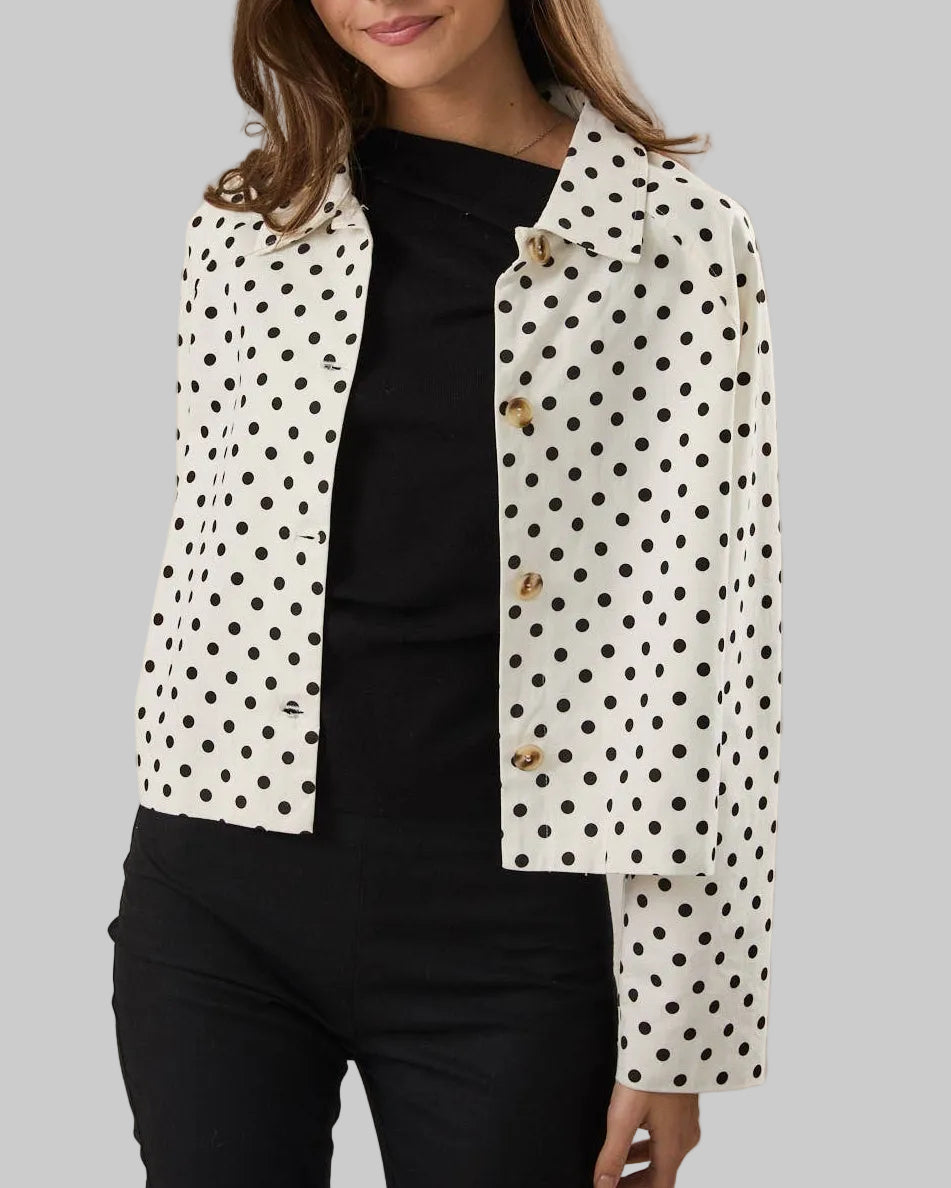 Woman wearing a polka dot jacket over a black top on a neutral background