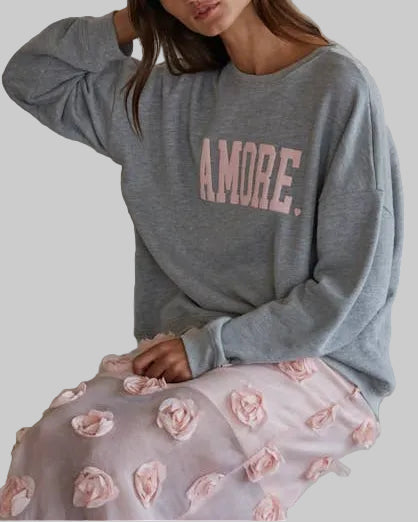 Woman wearing a gray sweatshirt with 'AMORE' text and a floral skirt sitting on steps.