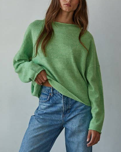 Woman wearing a green sweater and blue jeans against a plain background