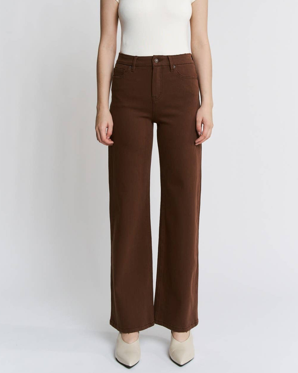 Woman wearing a white top and brown pants on a light gray background