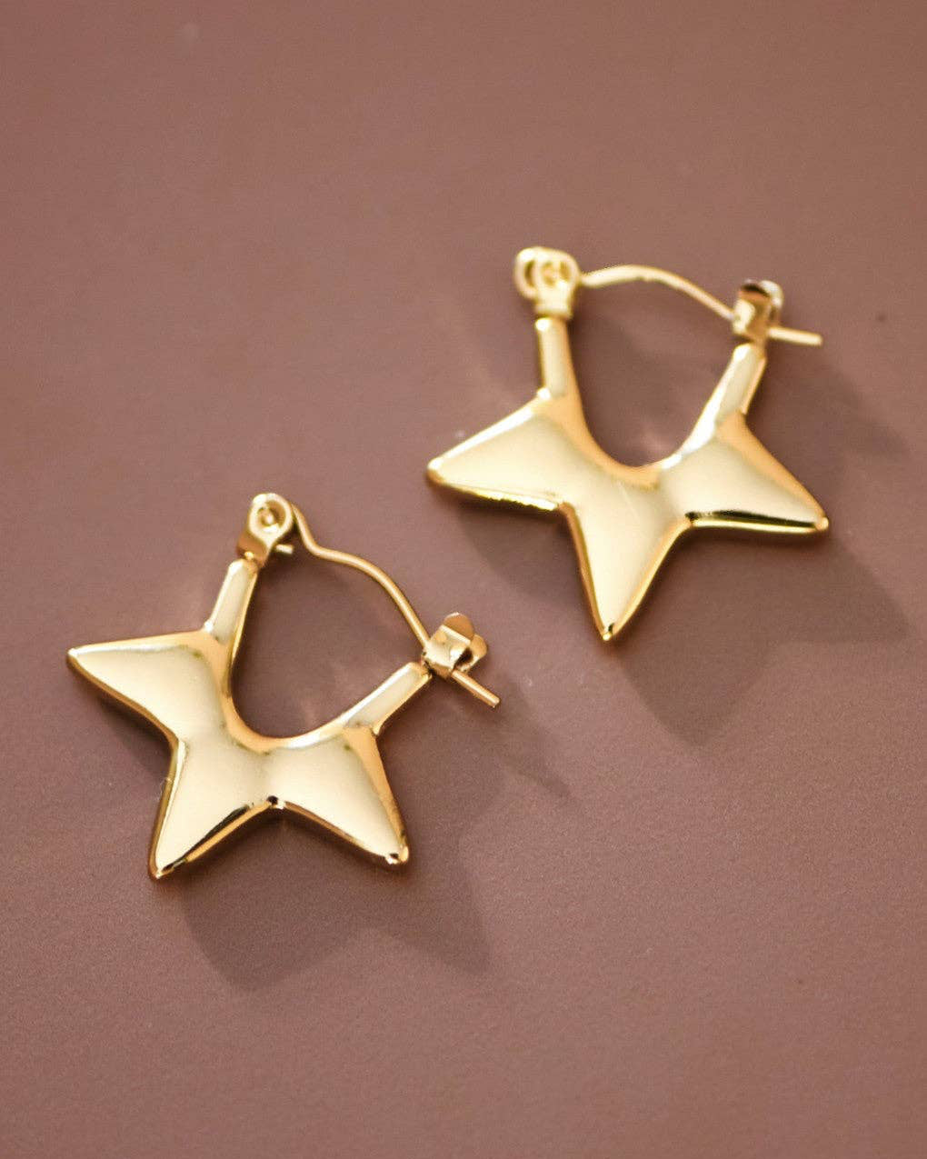 Gold star-shaped earrings on a brown background