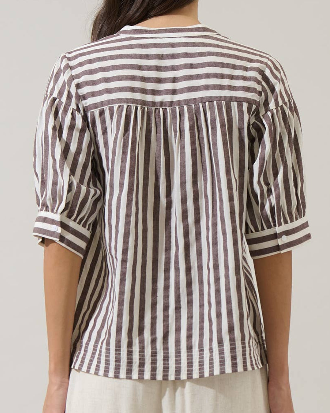 Person wearing a striped shirt and beige pants against a plain background