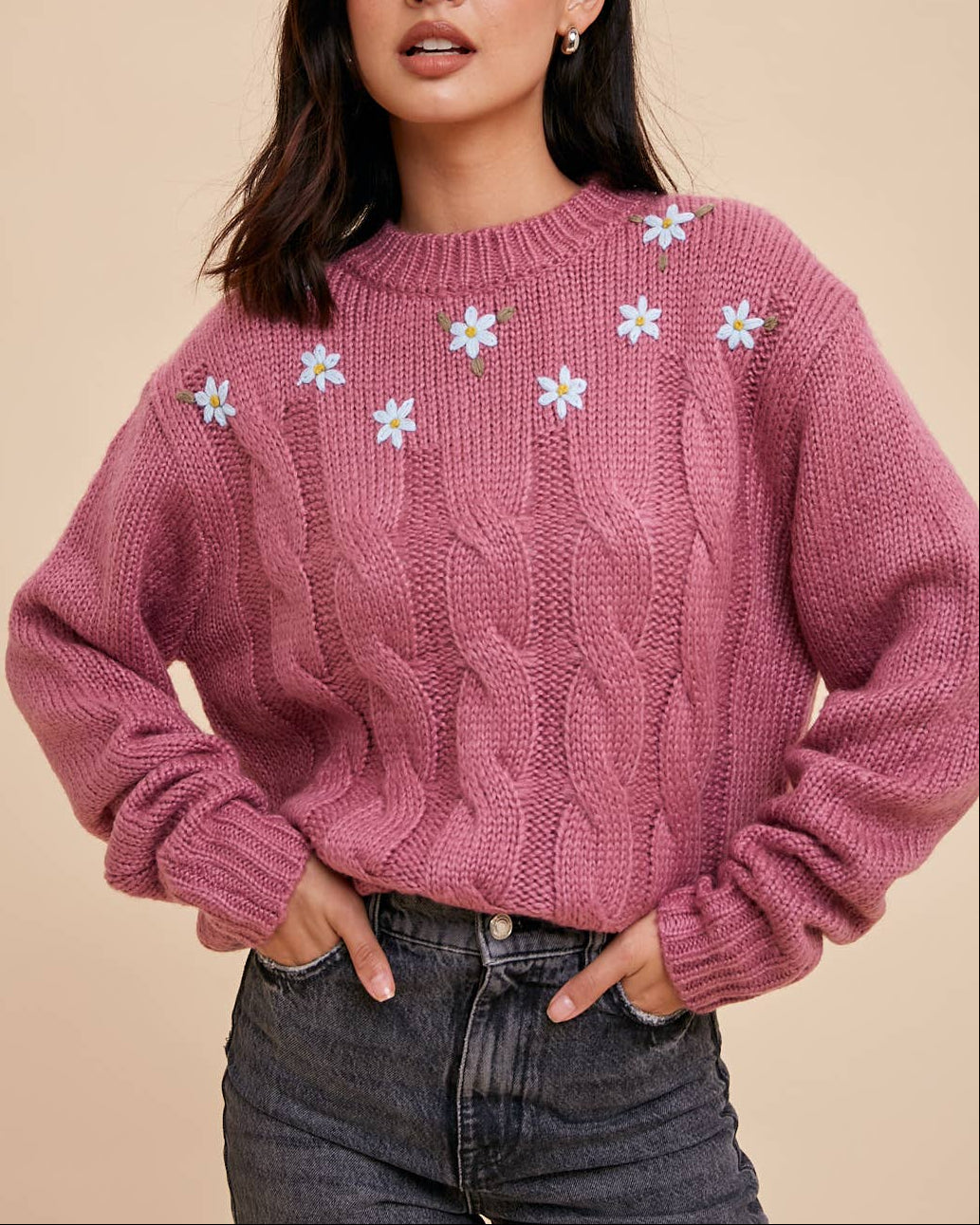 Woman wearing a pink sweater with floral patterns on a beige background