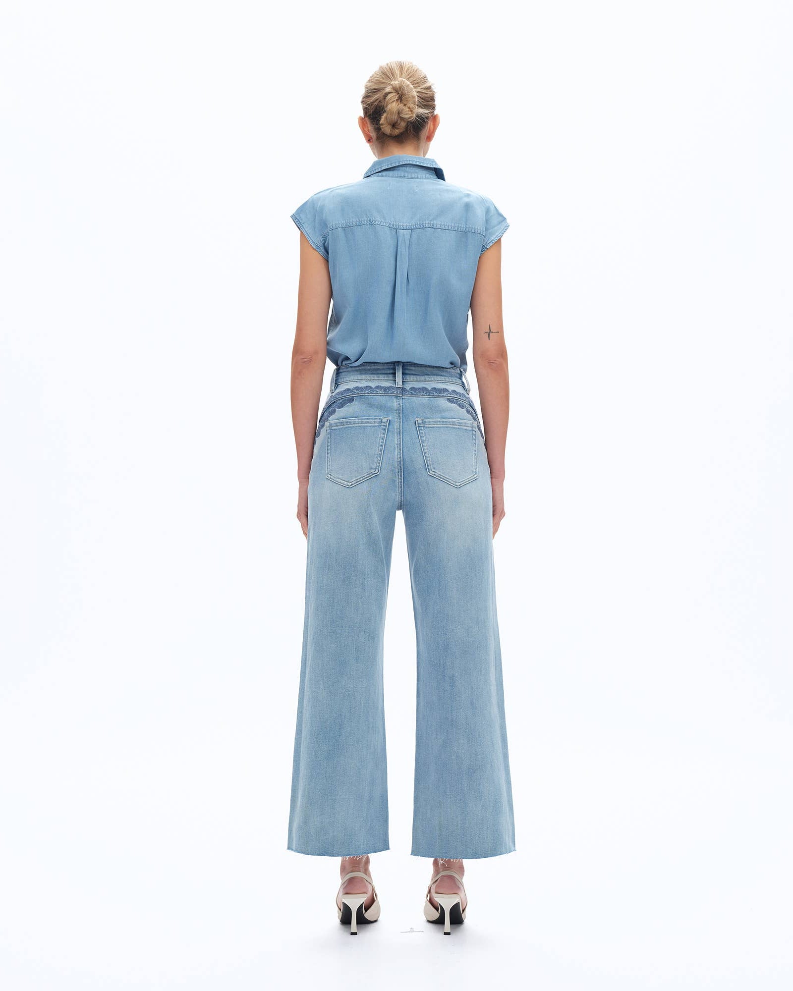 Person wearing a light blue sleeveless top and high-waisted jeans on a white background