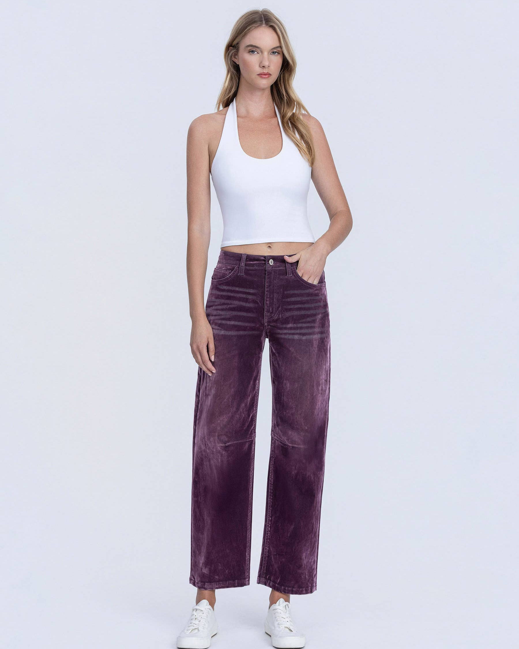 Woman wearing a white tank top and purple velvet pants on a white background