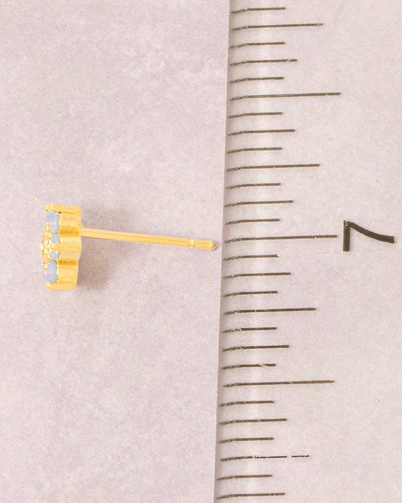 Gold stud earring next to a ruler on a light pink background
