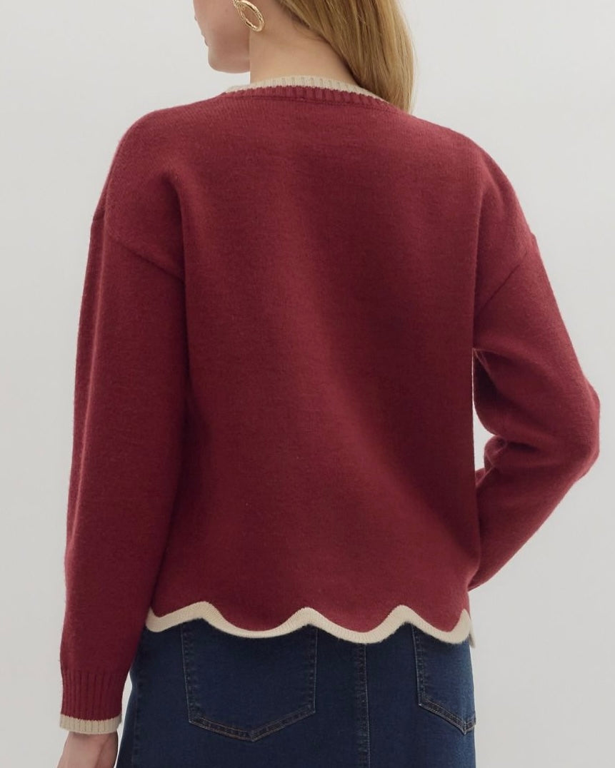 Person wearing a maroon sweater with scalloped hem on a plain background